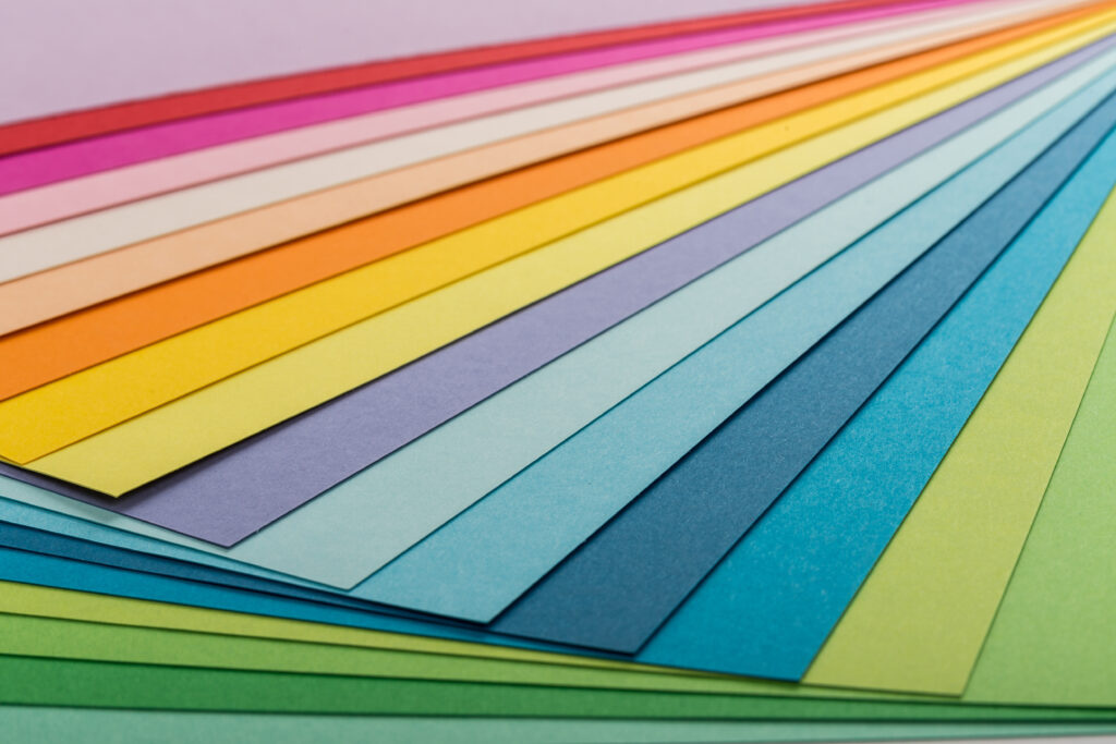 Stacked sheets of assorted colored paper stock arranged in a gradient of bright and pastel colors.