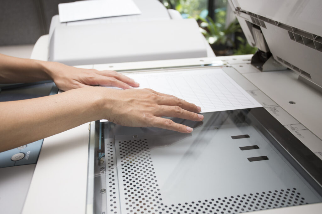 Hands aligning a document on the glass of a copier during small-format printing or scanning.