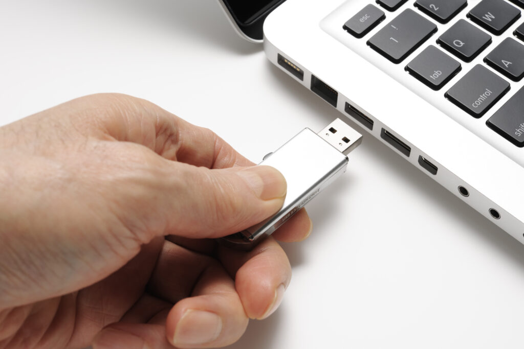 A hand inserting a USB flash drive into a laptop computer to transfer or print digital files.